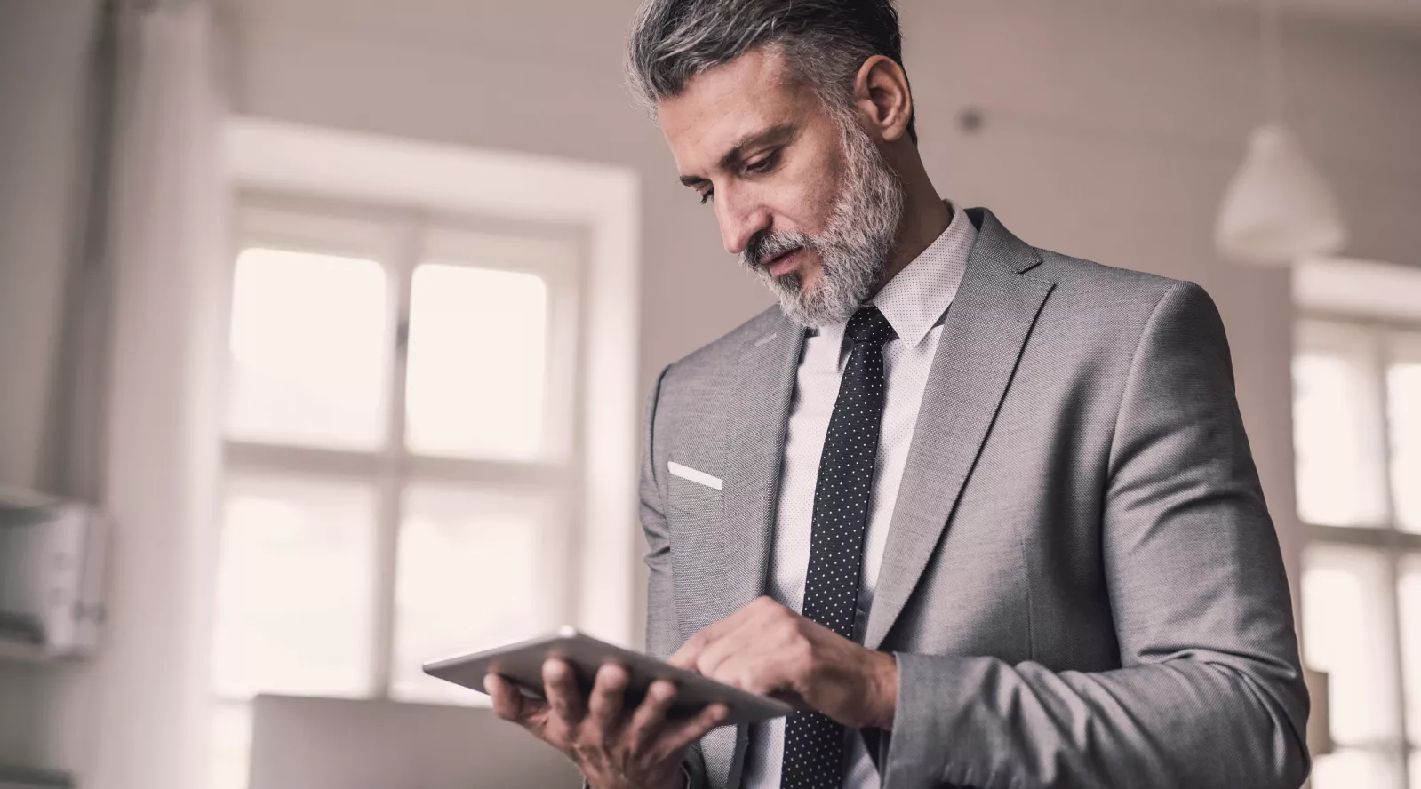 Un uomo in abito lavora su un tablet in un ufficio luminoso.